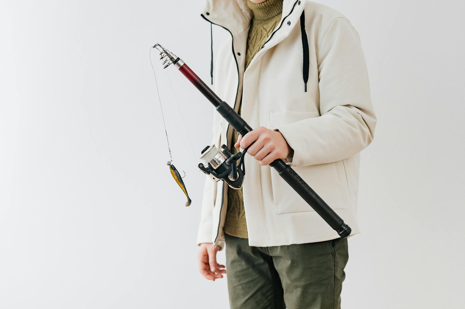 Person in a white jacket holding a fishing rod with lure against a neutral background.